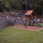 playground in backyard with stone wall